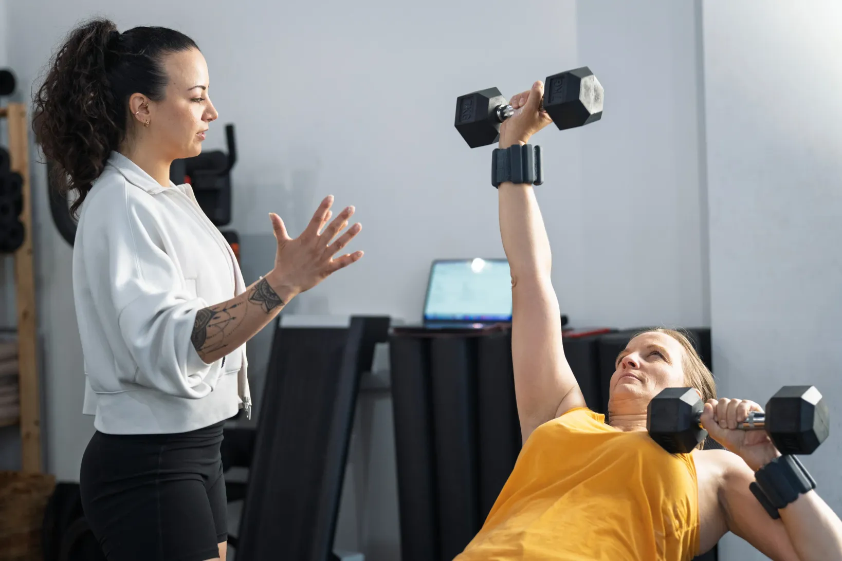 Coach guiding a client through a dumbbell press on a bench