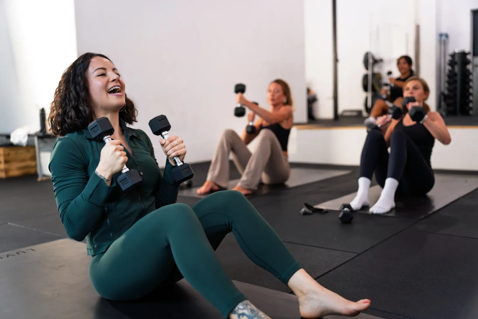 Coach laughing with dumbbells in hand while the group trains behind her