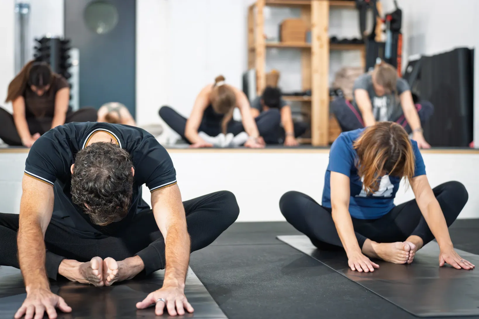 Two participants in a forward fold, with the group stretching behind them